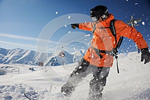 Professional snowboarder in orange sportswear riding down a mountain slope