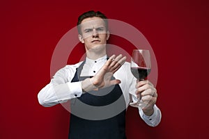 Professional sommelier with a glass of red bad wine refuses to drink on a red background, the guy the waiter does not recommend