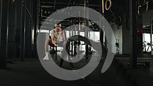 Professional sportsman bodybuilder powerful Caucasian man exercise battle ropes waves in sport gym. Fit guy training