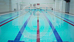 Professional sporty swimmer hardly working out in indoor empty pool jumping and swimming across track