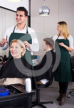 Professional stylist cutting hair of elderly blonde