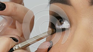 Professional stylist make-up artist makes up the smoky eye of an Asian girl model face in visage studio close up view