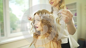 Professional stylist salon hairdresser putting jewelry hair accesory diadem pearl tiara on blonde wavy female model head