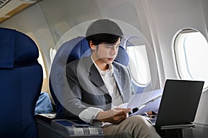 Professional and successful Asian businessman working during the flight for his business trip