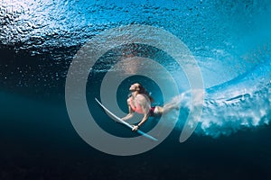 Professional surfer woman with surfboard dive underwater with under big ocean wave.