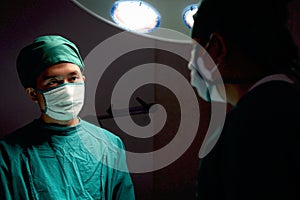 Professional surgeon doctor standing under bright light, using surgical equipment to do surgery at hospital operating room.