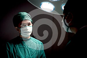 Professional surgeon doctor standing under bright light, using surgical equipment to do surgery at hospital operating room.