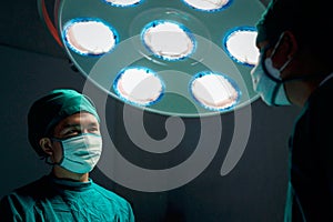 Professional surgeon doctor standing under bright light, using surgical equipment to do surgery at hospital operating room.