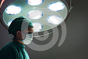 Professional surgeon doctor standing under bright light, using surgical equipment to do surgery at hospital operating room.