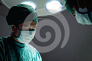 Professional surgeon doctor standing under bright light, using surgical equipment to do surgery at hospital operating room.