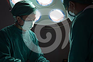 Professional surgeon doctor standing under bright light, using surgical equipment to do surgery at hospital operating room.