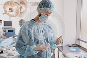 Professional surgeon in mask and gloves looking on his hands standing in operation room