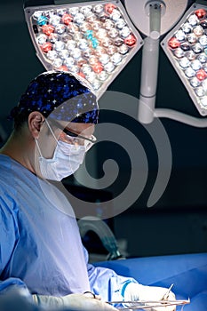 A professional surgeon in tension sews up a wound in the operating room, a modern medical light shines on him, a male