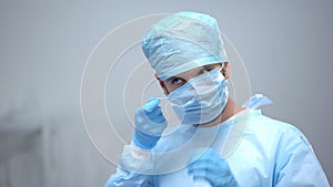 Professional surgeon in uniform wearing medical face mask before operation