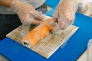 Professional sushi chef preparing roll at commercial kitchen. Cook puts the salmon on roll. Japanese cuisine recipes