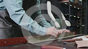 Professional tanner man puts paste on edge of a belt in workshop. Working process of the leather belt in the leather