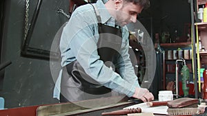 Professional tanner man puts paste on edge of a belt in workshop. Working process of the leather belt in the leather