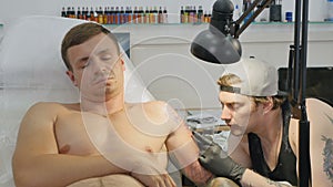 Professional tattoo artist makes the tattoo on man`s hand in tattoo salon