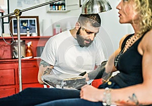 Professional bearded tattooer preparing blond woman for special tattoo session inside ink trendy studio  - Skin fashion concept - photo