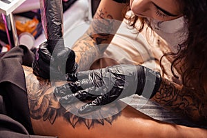 Professional tattooist creating black and white flower design on female thigh
