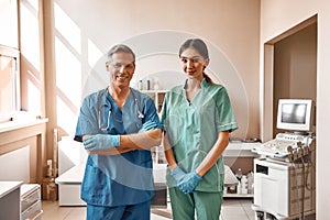 Professional team. Two positive vets in work uniform are smiling and looking at camera while standing at the veterinary