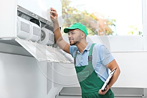 Professional technician with clipboard maintaining modern air conditioner