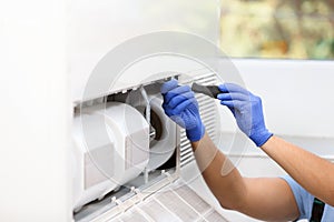 Professional technician maintaining modern air conditioner indoors, closeup.