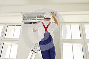 Professional technician worker is checking up, testing, repairing air conditioner indoors.