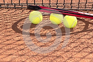Professional tennis racket and balls on an orange clay tennis court and net shadow. Set for playing tennis. Copy space