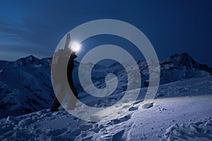 Professional tourist commit climb on great snowy mountain at night. Wearing backpack, headlamp and ski wear. Backcountry.