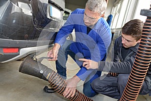 professional trainer teaching student how to fix car exhaust pipe