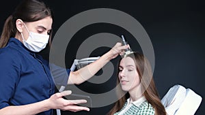 A professional trichologist examines a young woman's head using a dermatoscope.