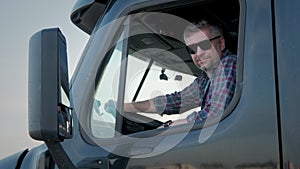 Professional Truck Driver sits in his truck and Behind Him Parked Long Haul Semi-Truck