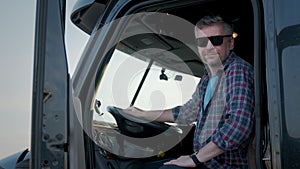 Professional Truck Driver sits in his truck and Behind Him Parked Long Haul Semi-Truck. Close up footage