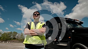 Professional Truck Driver in a yellow waistcoat approaches his truck and crosses his arms Behind Him Parked Long Haul