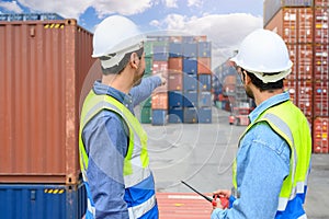 Professional of two Engineers or foreman container cargo wearing white hardhat and safety vests checking stock into container for