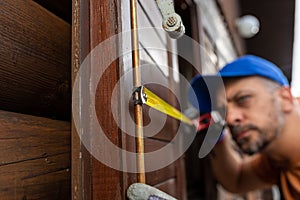 Professional using measure tape for window shutter replacement on wooden house. Home reparation concept