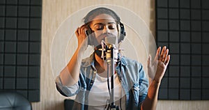 Professional vocal. Young black lady in headphones singing to microphone at sound record studio