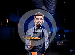 Professional waiter helpfully serves salad on a black background.