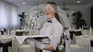 A professional waitress in white gloves holds a tray of champagne glasses.