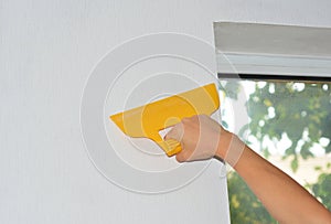 A professional wallpaper installer is wallpapering the wall around the window and removing air bubbles using a smoother tool