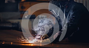 Professional welder in protective uniform with face mask, sparks fly apart, industrial welding close-up