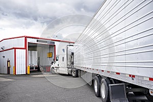 Professional white big rig semi truck with refrigerator semi trailer standing in line to truck repair and maintenance workshop