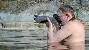 Professional wildlife photographer. A man with glasses stands in the water and looks into the viewfinder of the camera with a