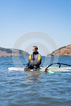 Portrait of windsurfer sitting on surfboard with sail in ocean