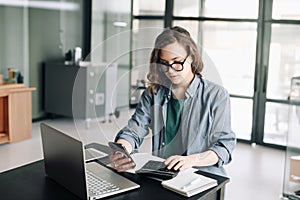 Professional woman accountant managing finances: using calculator and computer in office. Financial planning, budgeting