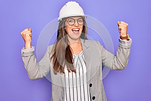 Professional woman engineer wearing industrial safety helmet over pruple background celebrating surprised and amazed for success