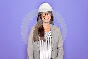 Professional woman engineer wearing industrial safety helmet over pruple background with a happy and cool smile on face