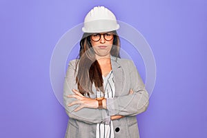 Professional woman engineer wearing industrial safety helmet over pruple background skeptic and nervous, disapproving expression