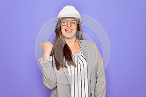 Professional woman engineer wearing industrial safety helmet over pruple background smiling with happy face looking and pointing